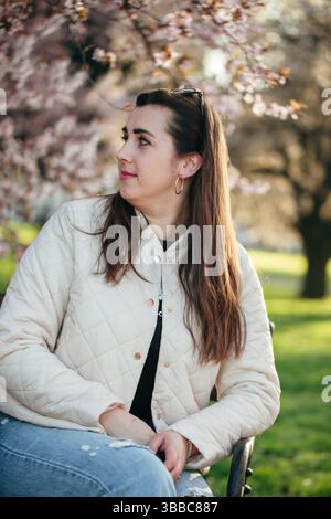 Die junge Frau sitzt anmutig unter blühenden Kirschblüten im Frühling in einem Park Stockfoto