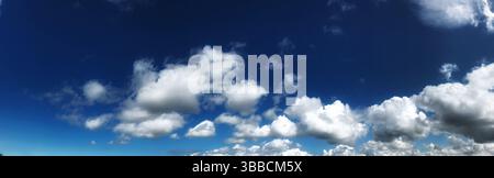 Ein Panoramafoto, das einen riesigen blauen Himmel mit flauschigen weißen Wolken zeigt und eine ruhige und weitläufige Atmosphäre schafft. Stockfoto