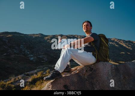 Ein junger Tourist mit Rucksack und Laptop sitzt auf dem Berg Stockfoto