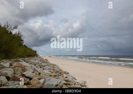 Karwia, Polen – 13. September 2020: Sturmwolken sammeln sich über der Ostsee, während Menschen am leeren Strand spazieren. Stockfoto