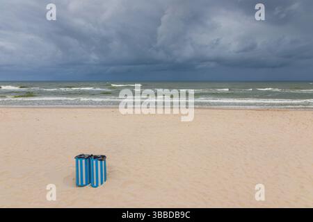 Zwei blau gestreifte Mülltonnen an einem einsamen Strand in Karwia, Polen, mit dramatischen Sturmwolken über der Ostsee. Stockfoto