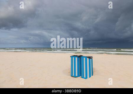 Zwei blau gestreifte Mülltonnen an einem einsamen Strand in Karwia, Polen, mit dramatischen Sturmwolken über der Ostsee. Stockfoto
