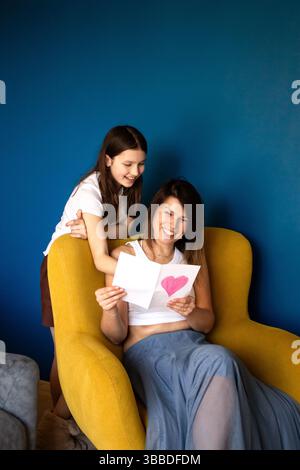 Frohe Muttertag. Die Tochter des Kindes gratuliert Müttern und schenkt ihr eine Geschenkbox und eine handgemachte Grußkarte Stockfoto