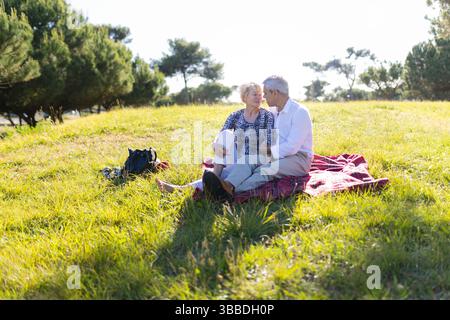 Seniorenpaar genießt ein romantisches Picknick im sonnigen Park auf Decke Stockfoto