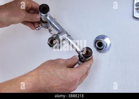 Entfernen des Vintage-Mischpults mit zwei Griffen von verdeckten Rohrleitungen in der Betonwand, fehlender Auslauf, freiliegende Gewindeeinlässe und Anzeichen für langfristigen Einsatz. Stockfoto