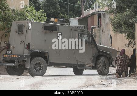 Nablus, Palästina. Mai 2025. Palästinensische Frauen weinen und knien während der Militäroperation in der Nähe israelischer Militärfahrzeuge. Die israelische Armee umzingelte ein Gebäude während einer Militäroperation, bei der fünf Palästinenser getötet wurden, die sich darin verbarrikadiert hatten. In der Stadt Tammun, nördlich des Jordantals im Westjordanland, brach ein Feuerwechsel zwischen Palästinensern und der israelischen Armee aus. Quelle: SOPA Images Limited/Alamy Live News Stockfoto
