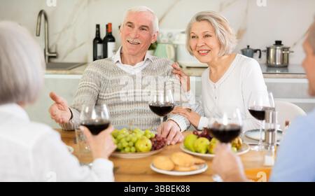 Zwei ältere Ehepaare sitzen am Tisch, genießen Essen und Wein, plaudern. Stockfoto