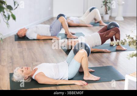 Aktive Frau, die während des Gruppentrainings in der Halle mit Pilates-Ball trainiert Stockfoto