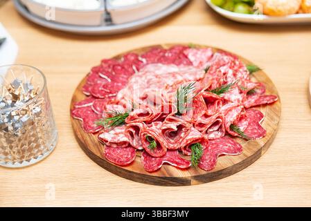 Holzbrett mit einer Auswahl an geschnittenem Wurstaufschnitt einschließlich Salami und Schinken, garniert mit frischem Dill zum Servieren. Stockfoto