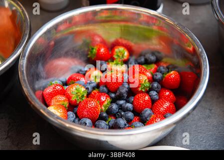 Nahaufnahme von frischen Erdbeeren und Heidelbeeren in einer Edelstahlschale, perfekt für gesunde Ernährung und Dessertzubereitung. Stockfoto