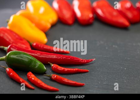 Rote, orange und gelbe Paprika und Chili, die einen Halbkreis auf einer dunklen Schieferoberfläche bilden Stockfoto