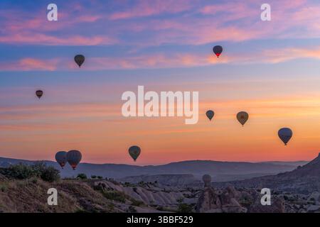 Mehrere Heißluftballons gleiten über dem pastellfarbenen Himmel über dem Love Valley, wo Kappadokiens felsige Türme eine surreale Landschaft schaffen. Stockfoto