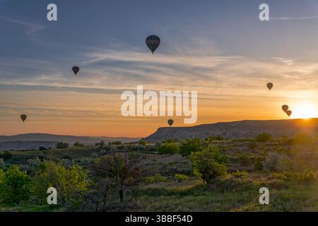 Ein einziger Heißluftballon schwingt über Love Valley in Kappadokien, während der goldene Sonnenaufgang lange Schatten über das zerklüftete Gelände wirft. Stockfoto