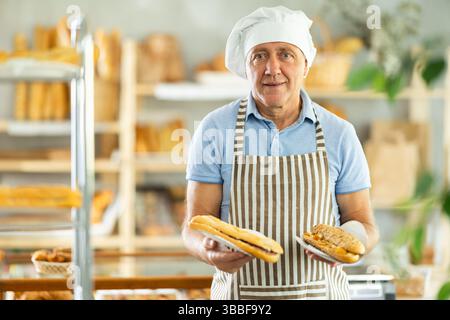 Älterer Mann Chef der Konditorei demonstriert Produkt aus Sortiment, Bocadillo auf Einwegplatten Stockfoto