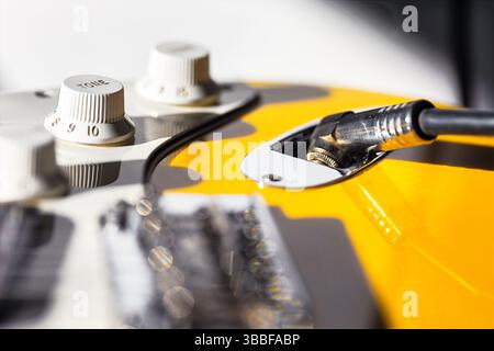 Gelbe E-Gitarre, die die Regler für Ton und Lautstärke sowie das eingesteckte Kabel hervorhebt. Streicher und Tonabnehmer im Vordergrund, Empha Stockfoto