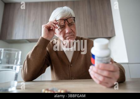 Älterer Mann liest Medikamentenetikett über Gläsern, um Dosierung und Gesundheitsanweisungen zu Hause zu überprüfen Stockfoto
