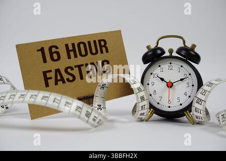 16-stündiger Fastentext mit Wecker und Messband auf weißem Hintergrund Stockfoto