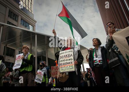 Nakba Day, Cambridge, Massachusetts, 15. Mai 2025. 50 bis 100 pro-palästinensische Demonstranten trafen sich vor der Haltestelle Kendall/mit T in der Nähe des Massachusetts Institute of Technology (mit). In Cambridge, neben Boston, befinden sich die Universitäten mit und Harvard. Eine 66-jährige Bostoner Frau (Mitte), die ein selbstgemachtes Schild trägt, schwingt eine palästinensische Flagge. T ist der Name für den Großraum Boston. Quelle: Chuck Nacke / Alamy Live News Stockfoto