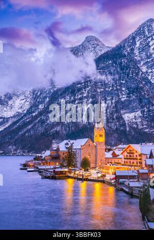 Hallstatt, Österreich. Ruhiges Alpendorf mit einem ruhigen See, schneebedeckten Dächern und einer atemberaubenden Bergkulisse während der Winterdämmerung. Stockfoto