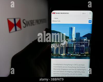 In dieser Abbildung hält eine Person ein Handy mit der Webseite des Immobilienunternehmens Swire Properties Limited auf dem Bildschirm vor dem Logo. Stockfoto