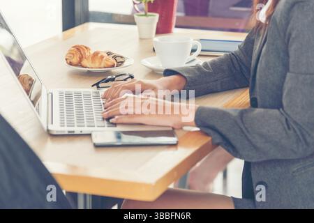 Seitenansicht einer jungen, arbeitenden Frau, die im Café, das vom Büro aus abgelegen ist, einen Laptop verwendet. Stockfoto