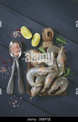 Frische rohe, weißfüßige Garnelen, Tigergarnelen vannamei, auf einem Holzschneidebrett, mit Limettenscheiben und Gewürzen Stockfoto