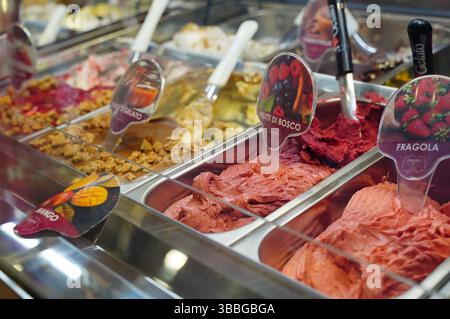 Nahaufnahme verschiedener farbenfroher Eisaromen in einer Vitrine in einer Eisdiele. Etiketten kennzeichnen Beeren-, Mango- und Erdbeersorten, Highlighti Stockfoto