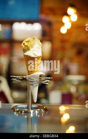 Ein Nahaufnahme eines köstlichen Eiskegels mit zwei Schaufeln, einer Vanille und einem Karamell, elegant präsentiert auf einem Metallständer in einem gemütlichen i Stockfoto