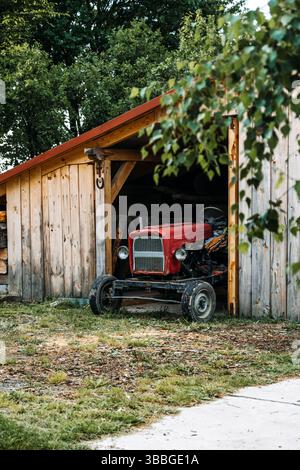 Ein Vintage-Traktor befindet sich unter einem hölzernen Unterschlupf, das Symbol für dauerhafte ländliche Praktiken und kleine Landwirtschaft. Stockfoto