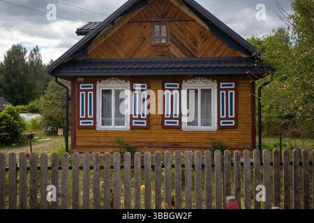 Ein kleines Haus mit einem Holzzaun und einer blau-weißen Zierleiste. Das Haus hat zwei Fenster und eine Veranda Stockfoto