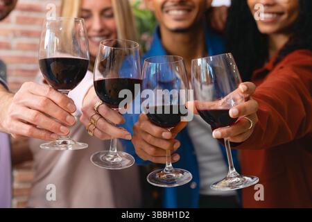 Multiethnische Gruppe glücklicher Freunde, die bei einem fröhlichen Treffen mit Rotwein tosten Stockfoto