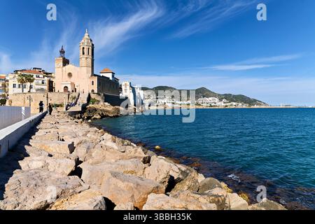 Sitges Spanien Kirche mit Blick auf das Mittelmeer mit Menschen, die entlang der Promenade spazieren gehen Stockfoto