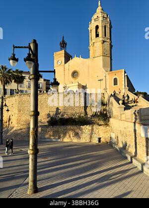 Sitges Spanien Kirche mit Blick auf das Mittelmeer mit Menschen, die entlang der Promenade spazieren gehen Stockfoto