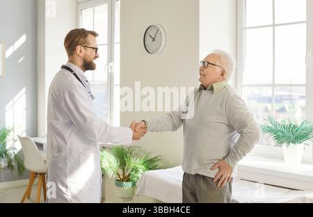 Freundlicher Arzt schüttelt die Hände mit einem älteren Patienten, der in der medizinischen Klinik steht Stockfoto