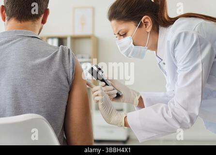 Ärztin untersucht die Handhaut eines jungen Mannes mit Lupe. Stockfoto