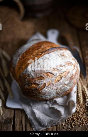 Gebräuntes, knuspriges Sauerteigbrot mit gerissener Oberseite und fester Kruste auf einem Vintage Holztisch. Herzhafte, im Ofen gebackene Runde in gemütlichem Bauernhaus Stockfoto