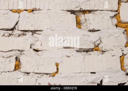 Weiße Ziegelwand mit gelbem Schaum in Rissen in der Wand, Ziegelwand als Hintergrund Stockfoto