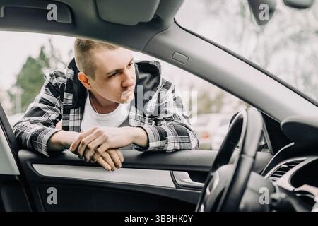 Junger Mann, der sich in lässiger Kleidung ins Autofenster lehnt Stockfoto