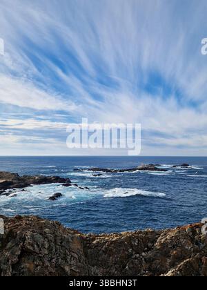 Blick auf die felsige Küste und die Wellen unter einem teilweise bewölkten Himmel Stockfoto