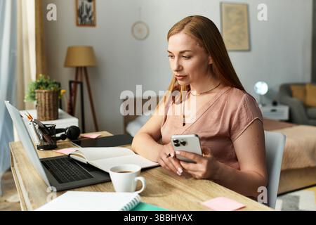Eine junge Frau sitzt leise an ihrem Schreibtisch und konzentriert sich auf Aufgaben mit einem warmen Getränk neben ihr. Stockfoto