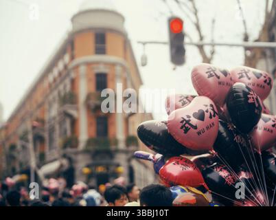 Herzförmige „Wuhan Love“-Ballons inmitten von Menschenmassen und kolonialer Architektur in einer Wuhan Street, Hubei, China Stockfoto