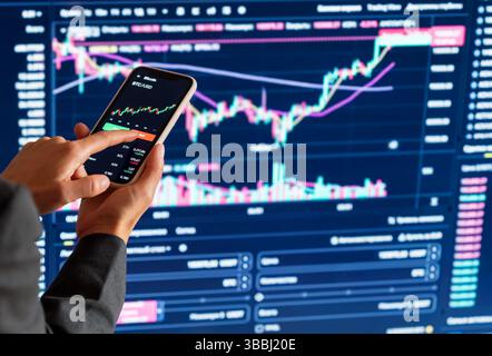 Geschäftsfrau analysiert Kryptowährungsmarkt auf Smartphone vor digitalen Handelsdiagrammen Stockfoto