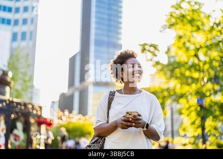 Lächelnde junge Frau, die das Handy in der Stadt benutzt Stockfoto