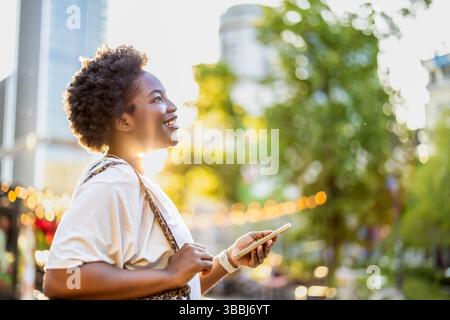 Lächelnde junge Frau, die das Handy in der Stadt benutzt Stockfoto