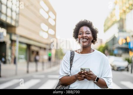 Lächelnde junge Frau, die das Handy in der Stadt benutzt Stockfoto