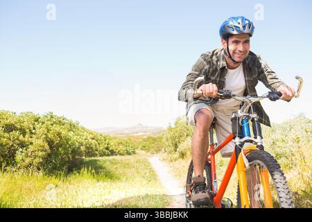 Radfahrer, der Fahrrad auf dem Feldweg mit orangem Rahmen, blauem Helm, Wasserflasche, Kopierraum in die Pedale tritt Stockfoto