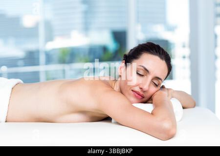 Entspannende Frau, die mit dem Gesicht nach unten auf dem Massagetisch im Spa-Raum lag, mit weißen Handtüchern und Glasfenstern Stockfoto