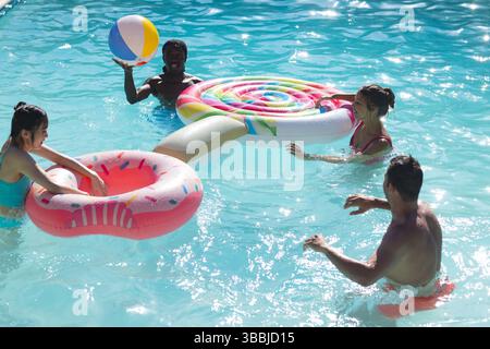 Schwimmende Freunde auf Donut und Lutscher schwimmen im Pool und halten Regenbogenbälle am Strand Stockfoto