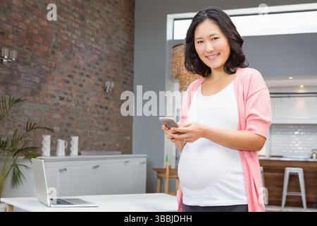 Smartphone auf weißem Tisch neben offenem Laptop, Pendelleuchte über Kücheninsel Stockfoto