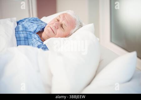 Ruhender Seniorenmann, der auf der Seite im Schlafzimmer liegt, mit weißer Bettdecke und blauem Pyjama, Kopierraum Stockfoto